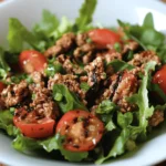 Grilled ground turkey patties served on a bed of fresh arugula, cherry tomatoes, and cucumbers in a black bowl.